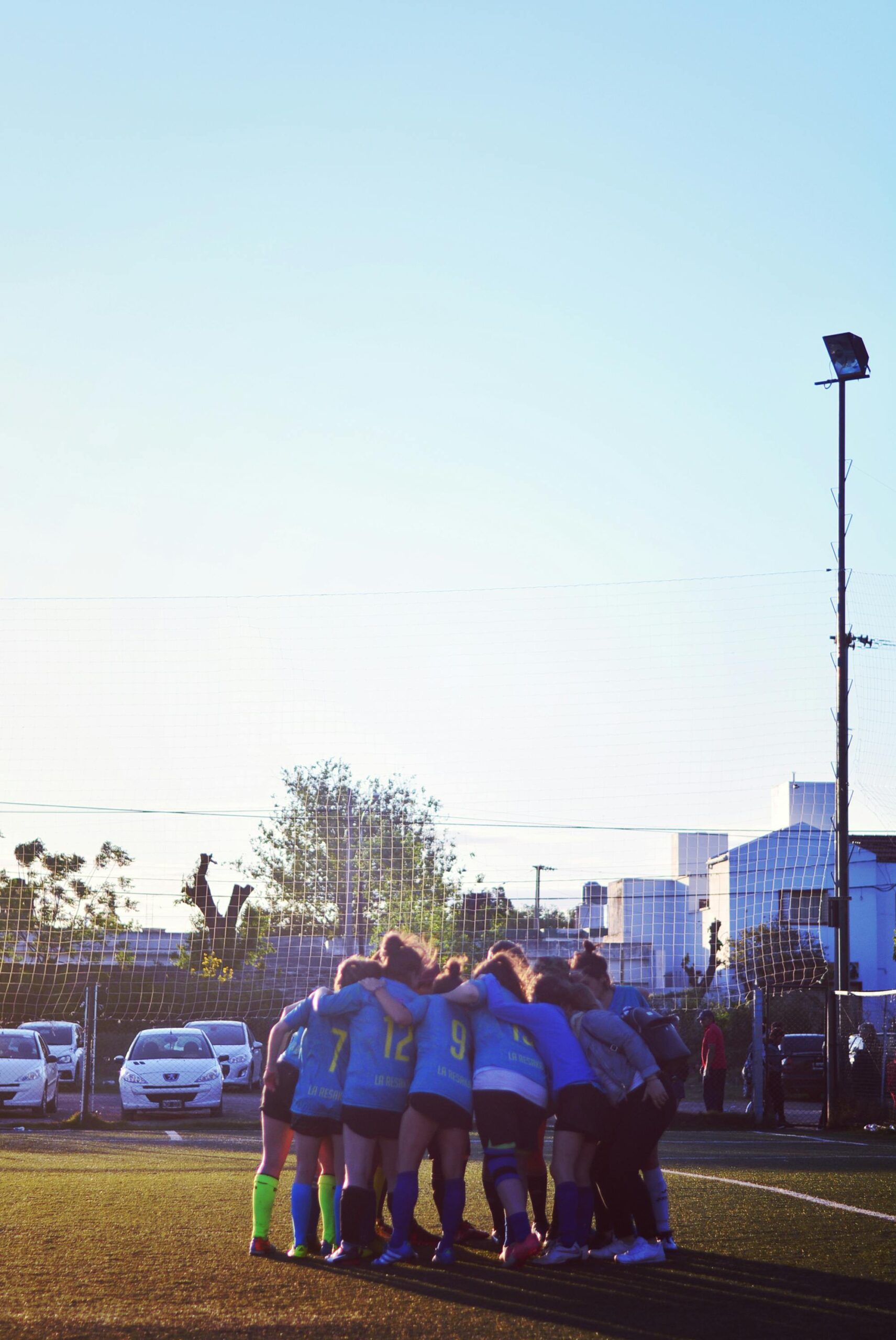A women's soccer team huddling on the field at sunset in Córdoba, Argentina.