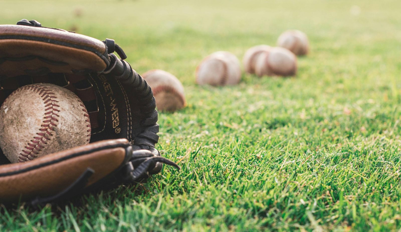 Baseball glove and balls on a green field, ready for outdoor pitching practice